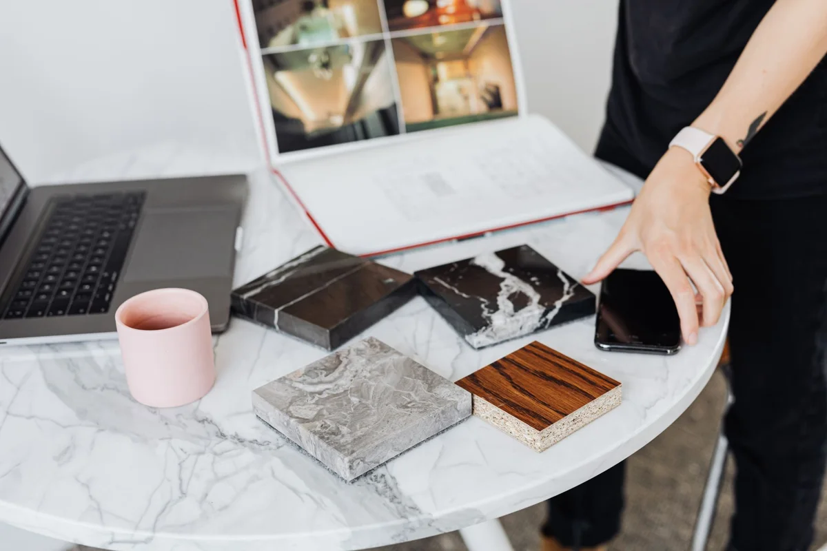 A hand beside timber and stone surface samples on a table
